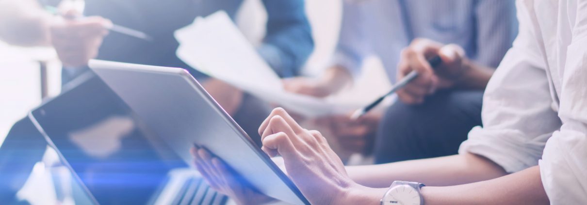 Closeup view of three young coworkers working on mobile laptop computer at office.Young woman holding tablet and pointing on touch screen. Horizontal, blurred background.Cropped.