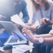 Closeup view of three young coworkers working on mobile laptop computer at office.Young woman holding tablet and pointing on touch screen. Horizontal, blurred background.Cropped.