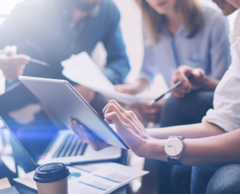 Closeup view of three young coworkers working on mobile laptop computer at office.Young woman holding tablet and pointing on touch screen. Horizontal, blurred background.Cropped.