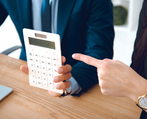 Zwei Personen in Geschäftskleidung halten und zeigen auf einen großen Taschenrechner.