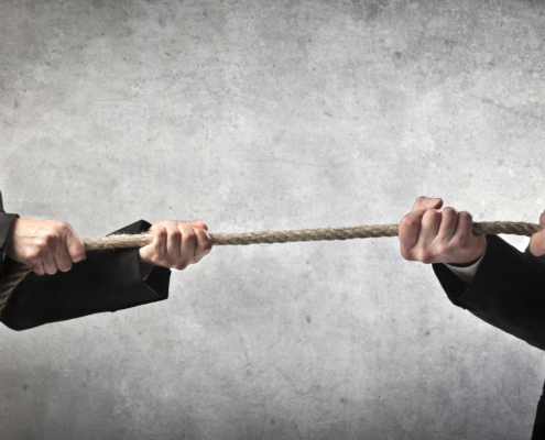 Zwei Personen in Anzügen ziehen an entgegengesetzten Enden eines Seils.