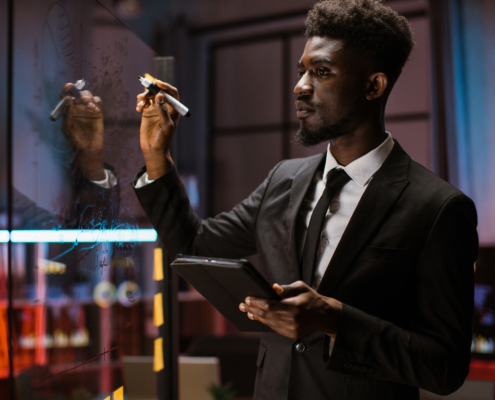 African american finance expert, using tablet while checking work plan, looking at scrum glass board