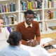 Gruppe von fünf Personen sitzt an einem Tisch in einer Bibliothek und arbeitet gemeinsam an einem Projekt.