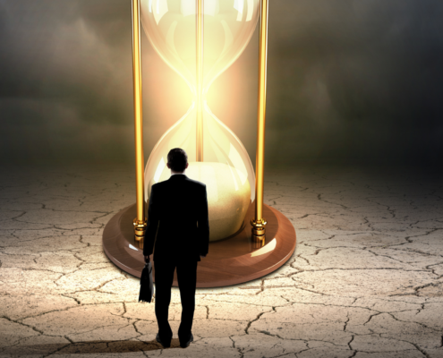 Person im Anzug steht vor einer großen, leuchtenden Sanduhr auf rissigem Boden.