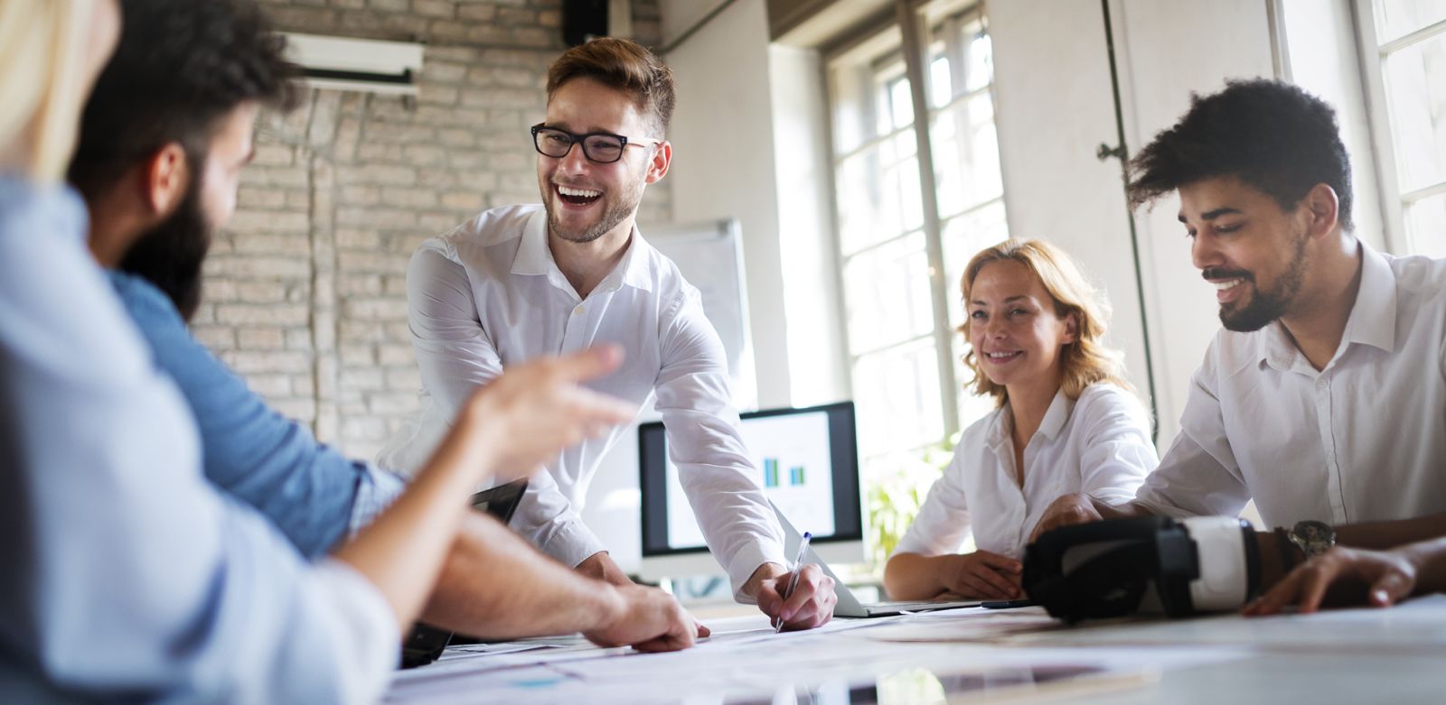Eine Gruppe von Menschen in einem Büro lacht und arbeitet zusammen an einem Tisch.