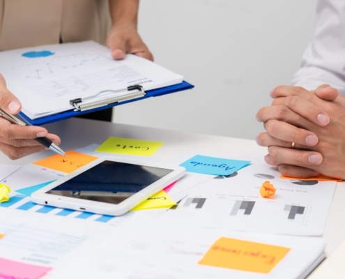 Zwei Personen arbeiten an einem Tisch mit Notizen, Diagrammen und einem Tablet.