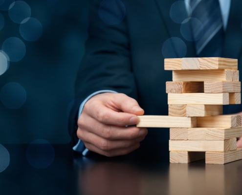 Geschäftsmann in Anzug spielt Jenga und zieht vorsichtig einen Holzklotz heraus.