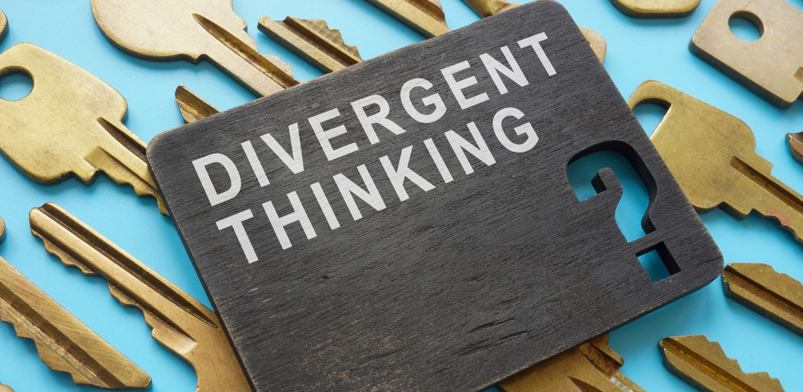 Schwarzes Schild mit der Aufschrift "Divergent Thinking" neben goldenen Schlüsseln auf blauem Hintergrund.