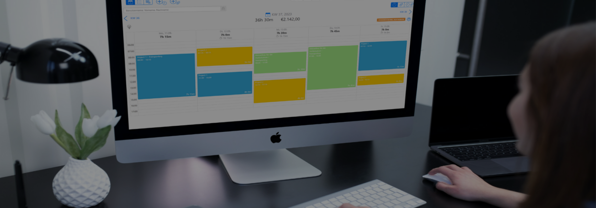 Eine Person arbeitet an einem Schreibtisch mit einem großen iMac, auf dessen Bildschirm eine TimeTrack Wochenansicht eines Kalenders mit farblich markierten Terminen angezeigt wird.
