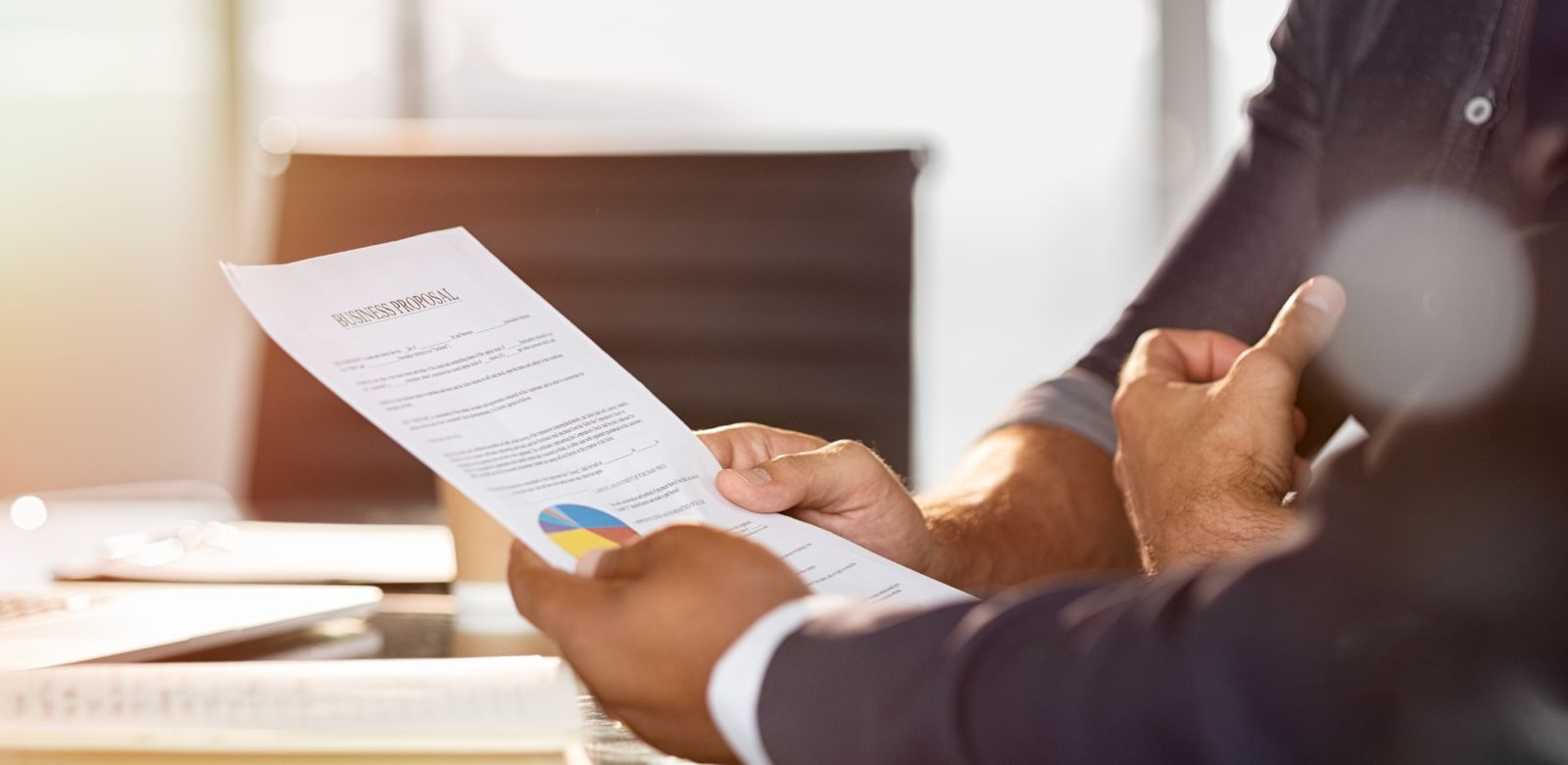 Zwei Personen betrachten ein Dokument mit der Aufschrift "Business Proposal" in einem Büro.