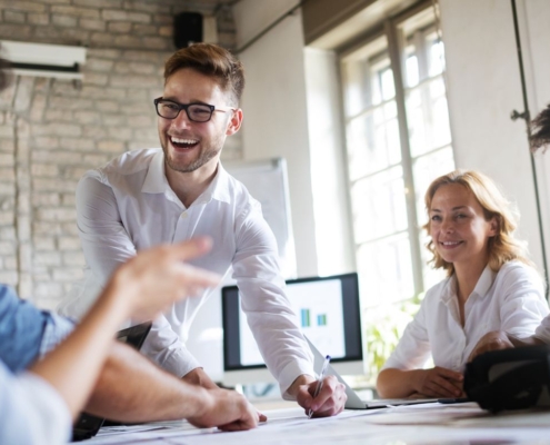 Eine Gruppe von Kollegen sitzt in einem Büro und lacht, während sie gemeinsam an einem Dokument arbeiten.
