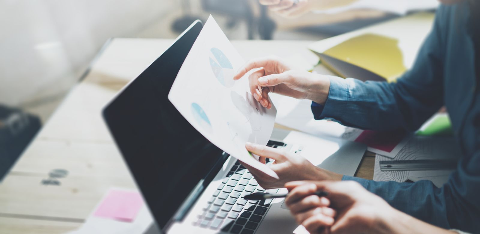 Zwei Personen arbeiten an einem Laptop und überprüfen ein Dokument mit Diagrammen.