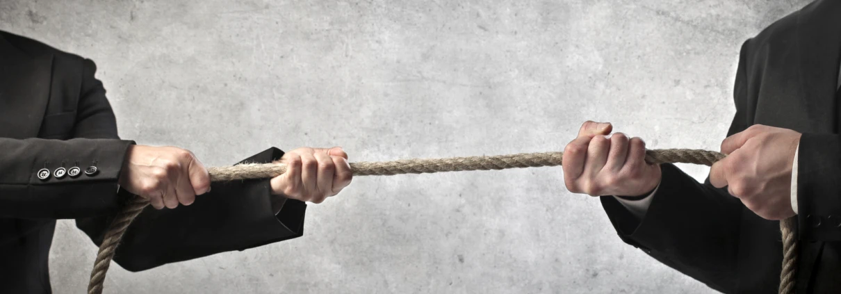 Zwei Personen in Anzügen ziehen an entgegengesetzten Enden eines Seils.