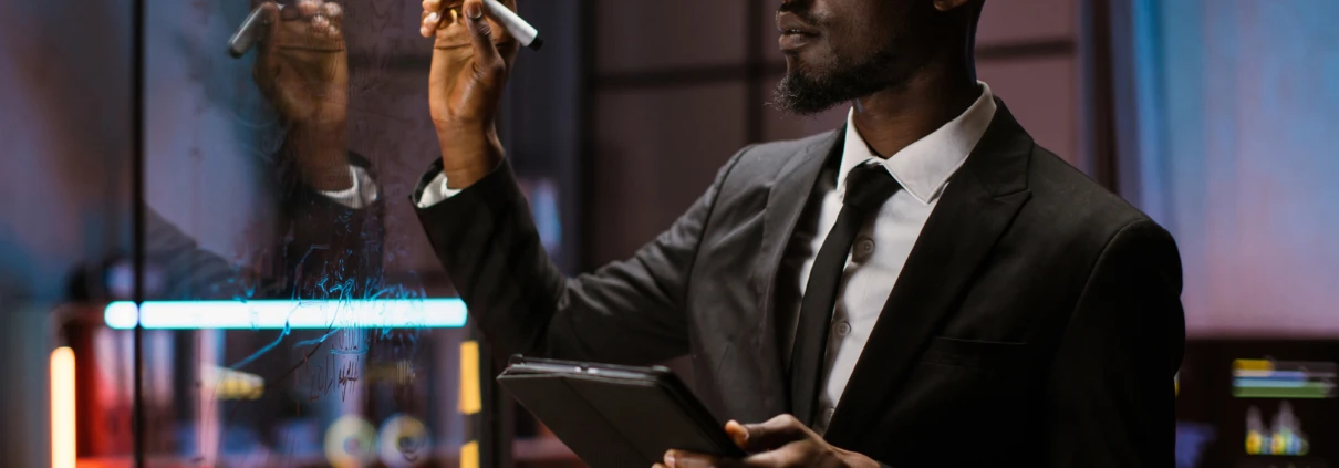 African american finance expert, using tablet while checking work plan, looking at scrum glass board