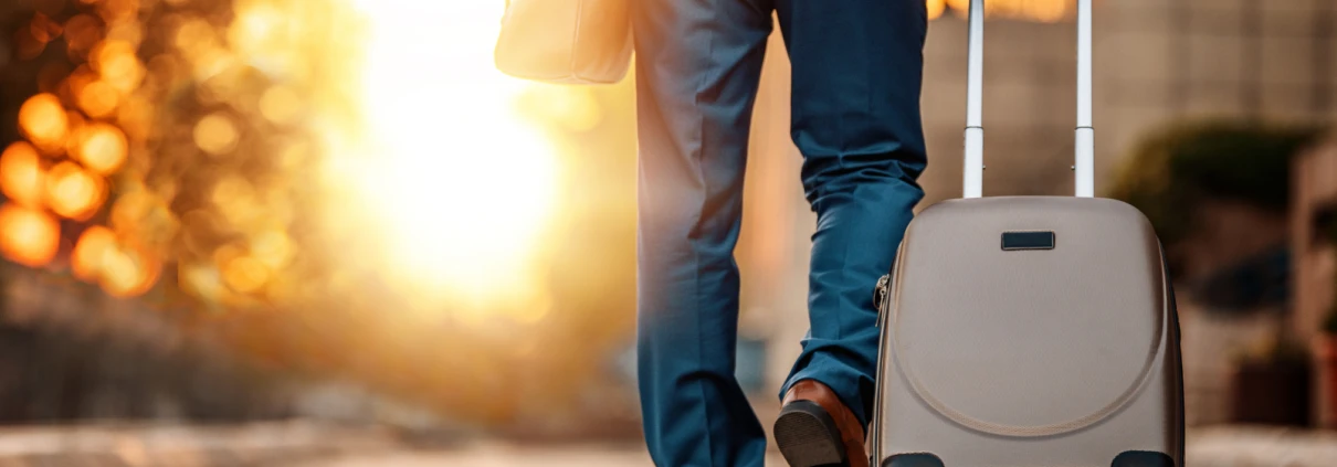 Person in einem Anzug, die bei Sonnenuntergang einen Rollkoffer zieht.